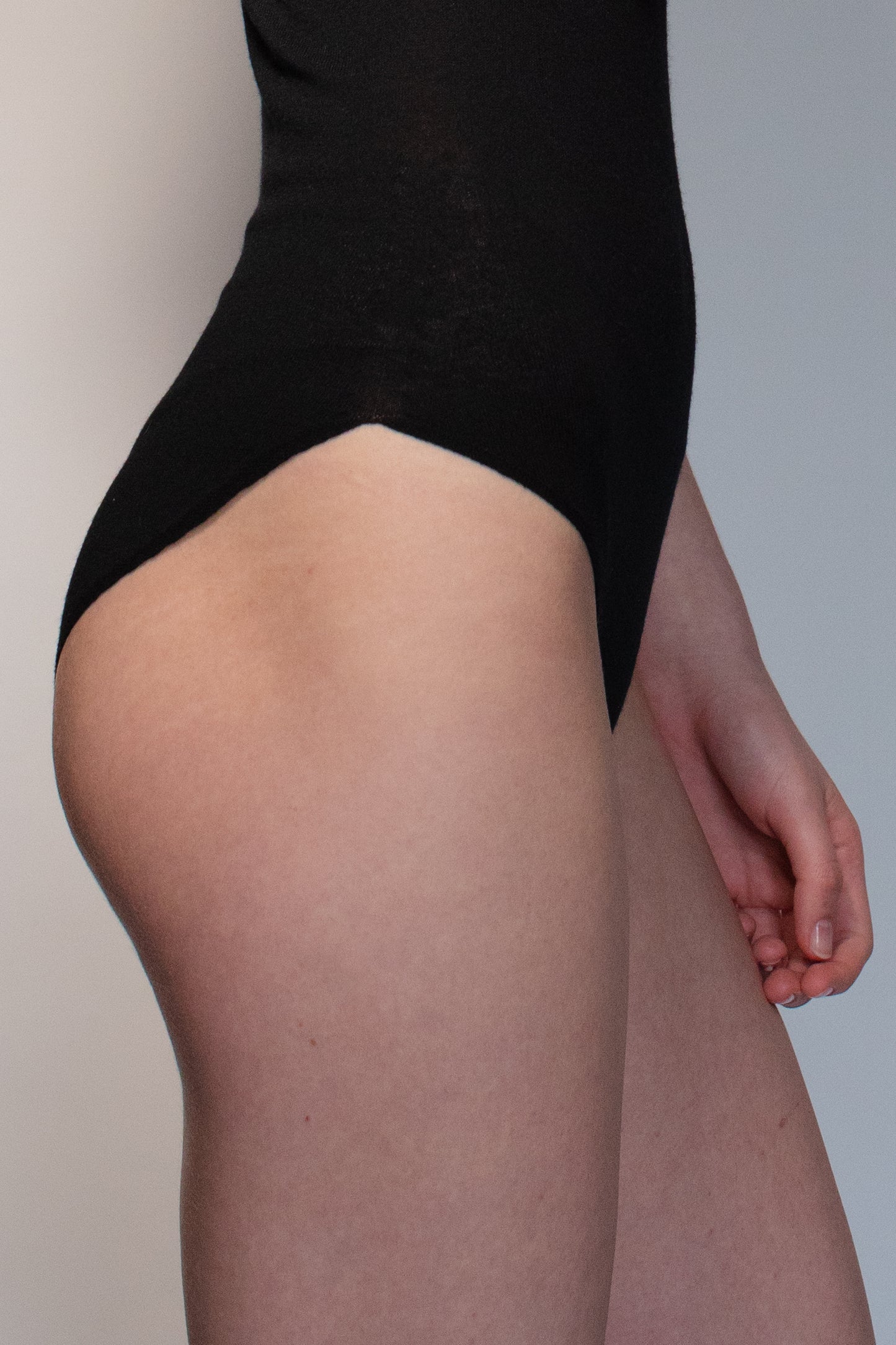 Side detail of black knit bodysuit with high-cut leg and sculpted fit. -farbe-schwarz