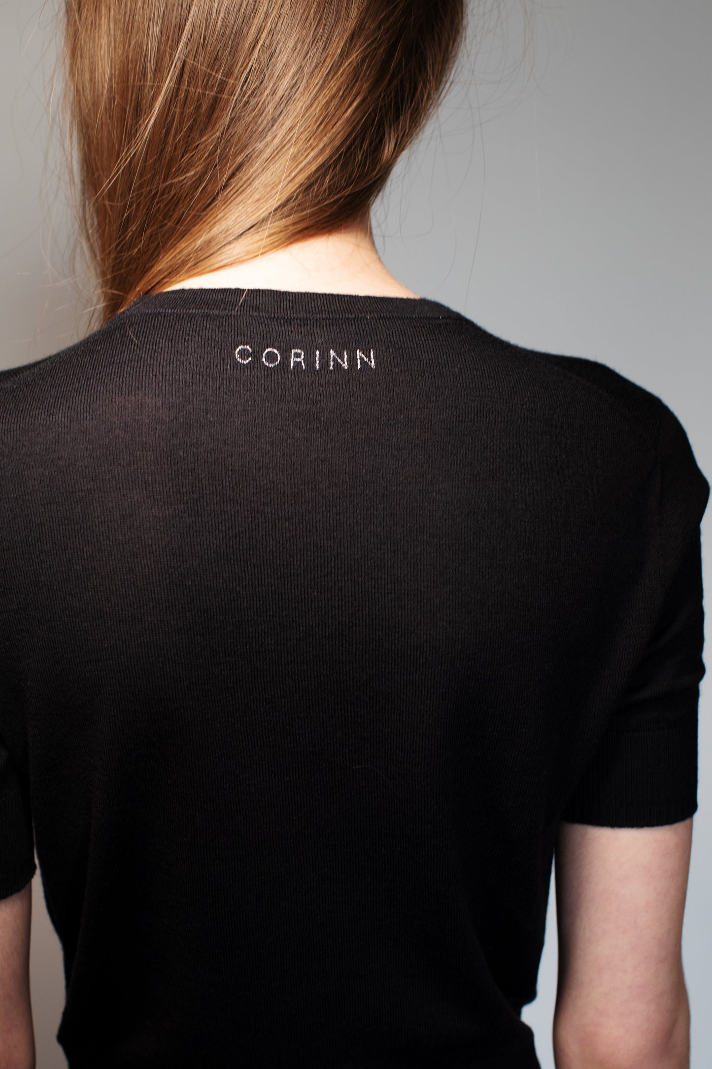 Back view of the CORINN seamless silk wool knit T-shirt in black with discreet CORINN embroidery below the neckline. farbe-schwarz