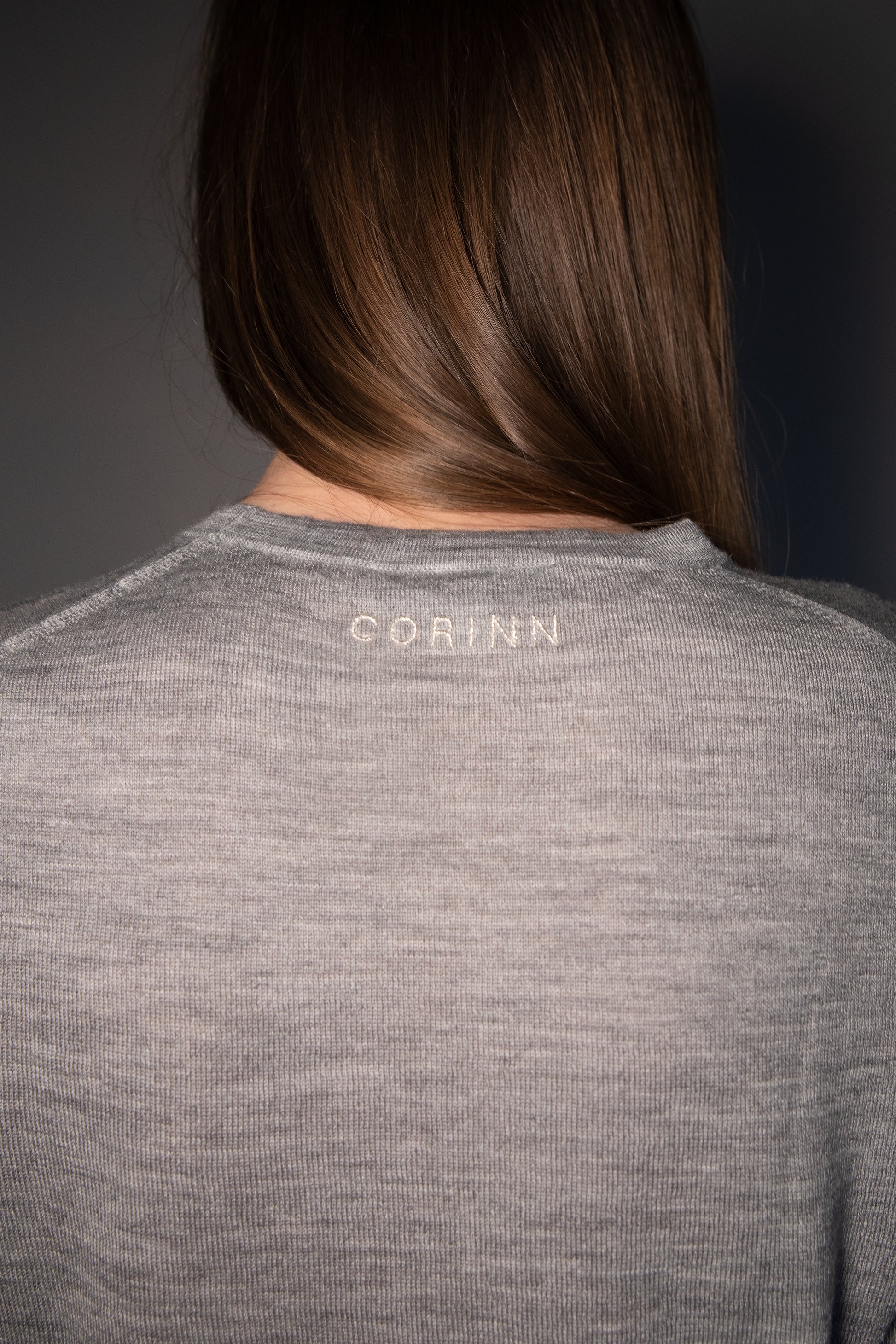 Back view of the CORINN seamless silk wool knit T-shirt in grey featuring subtle CORINN embroidery below the neckline. farbe-grau - melange